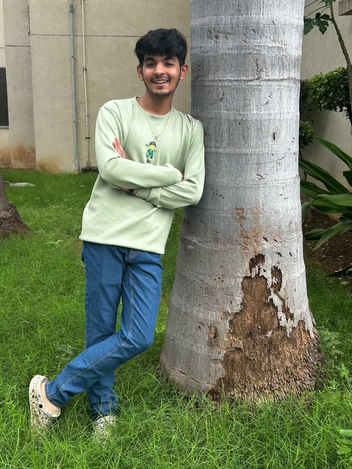 Romil Lodaya in a green sweatshirt, arms crossed, leaning against a palm tree and smiling