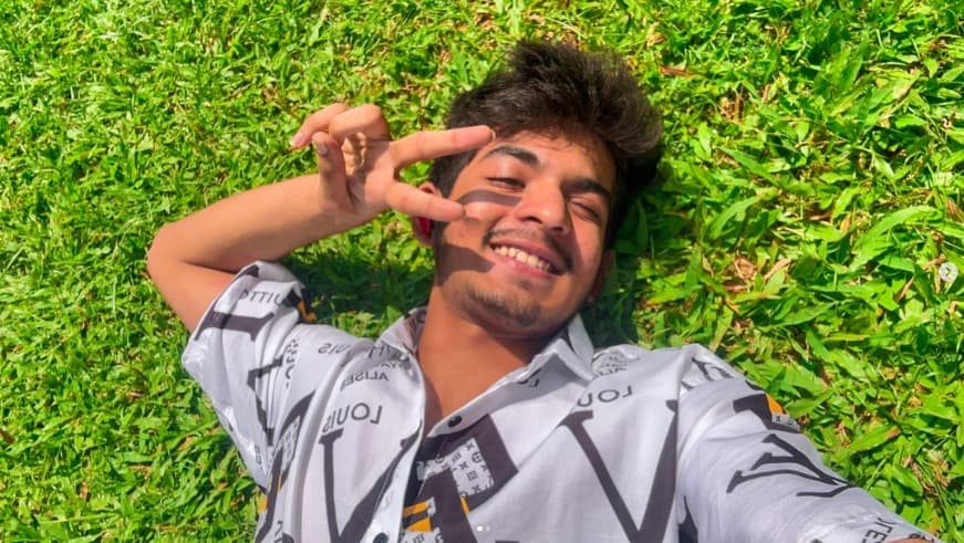 Romil Lodaya lying on grass in sunlight, smiling and making a peace sign