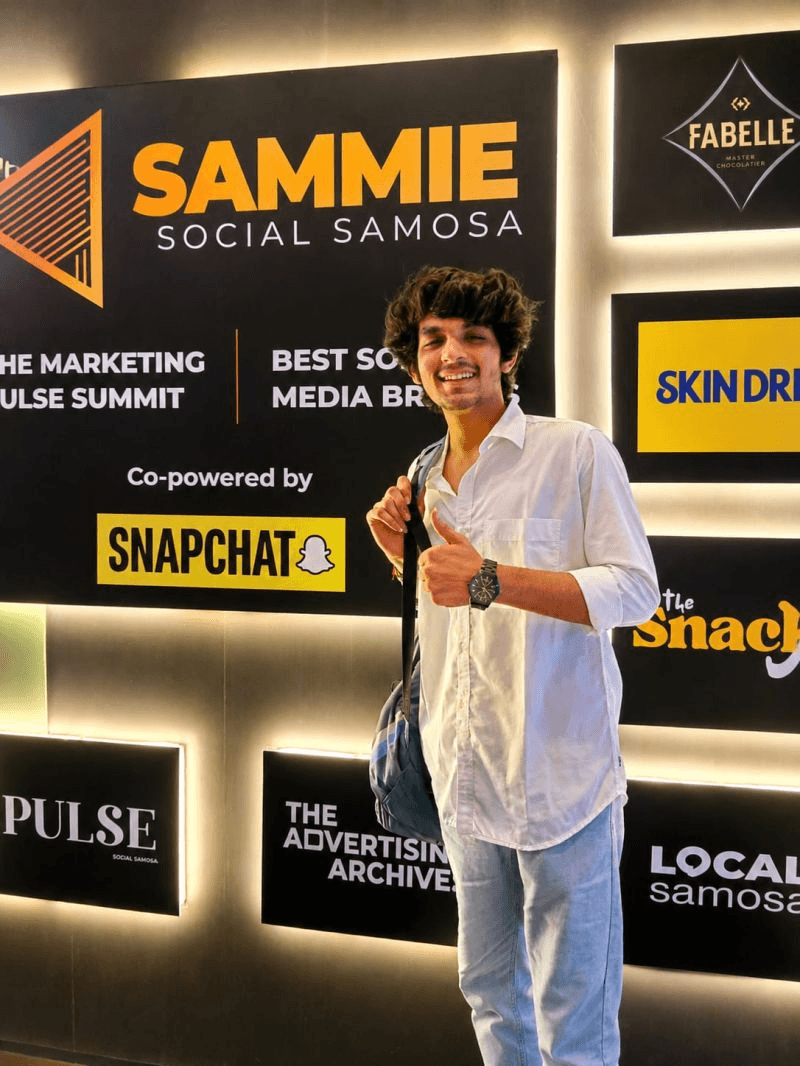 Romil Lodaya smiling and giving a thumbs up in front of the Sammie by Social Samosa summit display